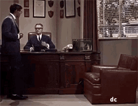a man in a suit is standing in front of a man sitting at a desk ..