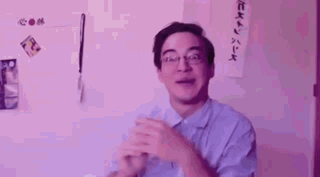 a man wearing glasses is clapping his hands in front of a wall with chinese writing .