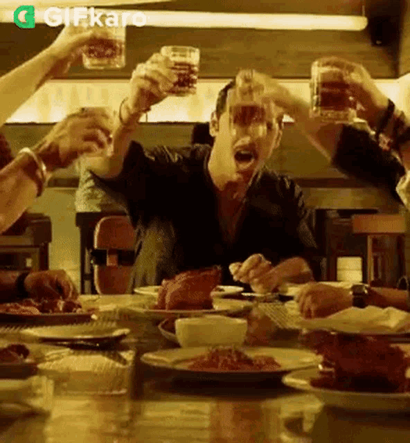 a group of people are sitting at a table eating food and toasting with beer glasses .