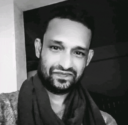 a man with a beard is wearing a scarf around his neck and looking at the camera .