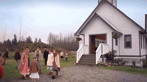 a group of people standing in front of a small white church