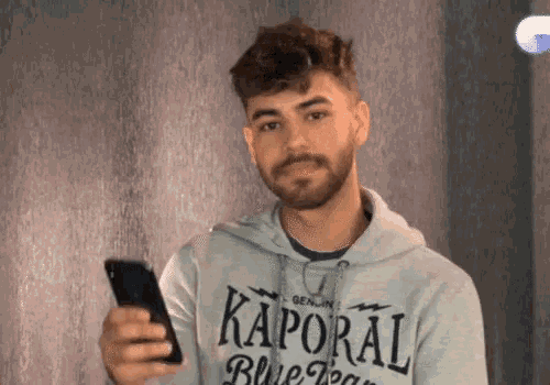 a man wearing a kaporal hoodie holds a cell phone
