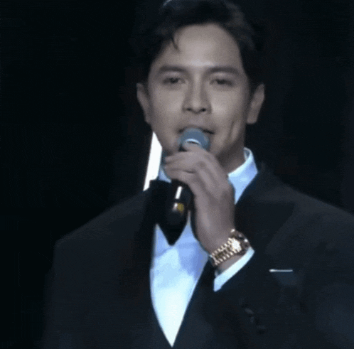 a man in a tuxedo is holding a microphone and wearing a watch