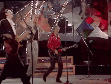 a man in a red jacket is playing a guitar in front of a microphone on a stage .