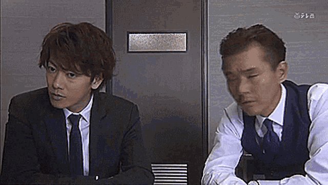 two men in suits and ties are sitting next to each other in front of a door that says lg on it