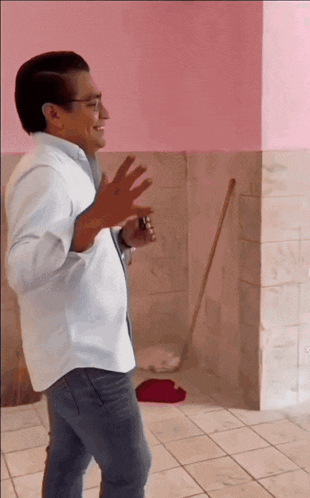 a man in a white shirt is dancing in front of a pink wall and a mop
