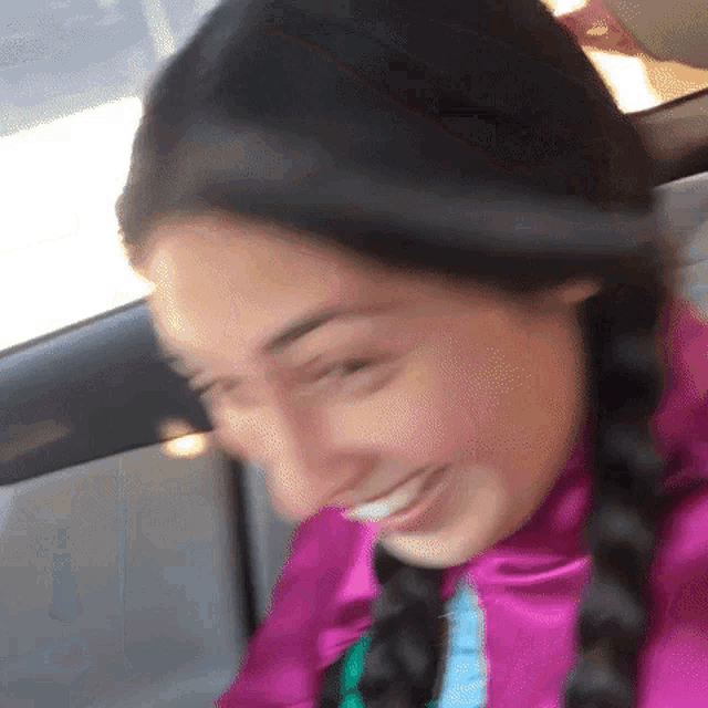 a woman wearing a pink jacket and braids is smiling in a car
