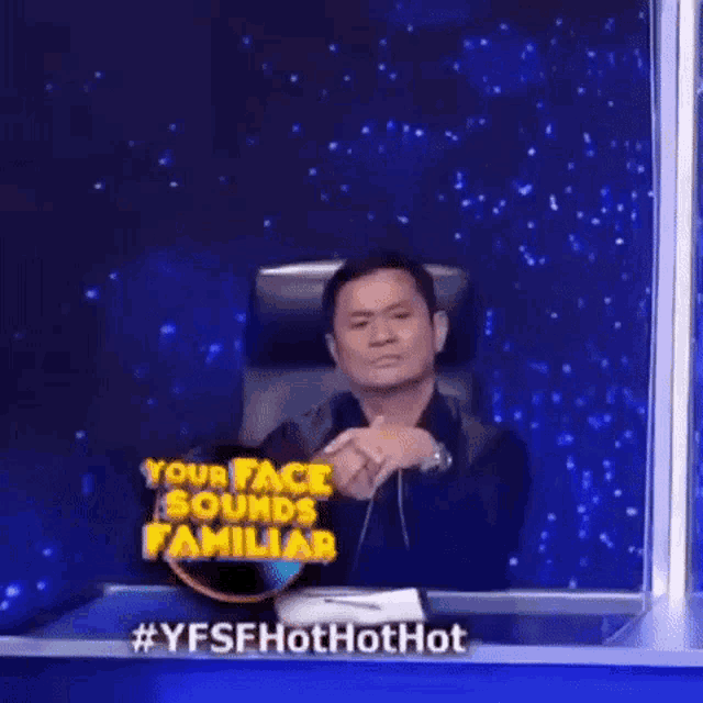 a man is sitting in front of a screen with a sign that says your face sounds familiar .