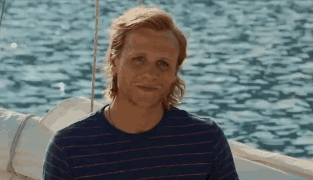 a man in a striped shirt is sitting on a boat in the water .