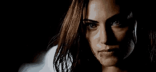 a woman with blood on her face is looking at the camera in a dark room .