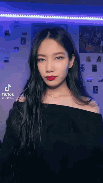 a woman in a black off the shoulder top with red lipstick is standing in front of a wall .