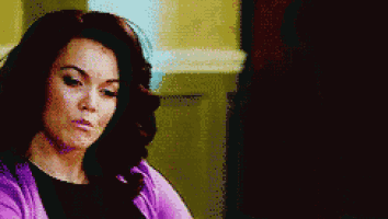 a woman with long dark hair is wearing a purple cardigan and a black shirt .