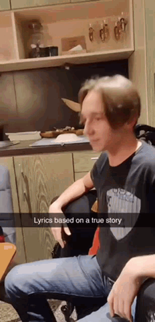 a man in a black shirt is sitting in front of a kitchen with lyrics based on a true story written on a snapchat