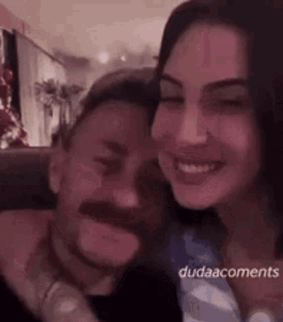 a man with a mustache is hugging a woman .