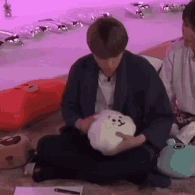 a man is holding a stuffed animal while sitting on the floor .