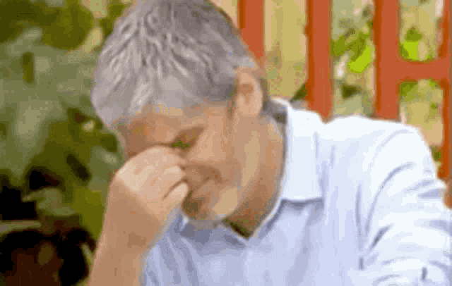 a man with gray hair is covering his nose with his hand .