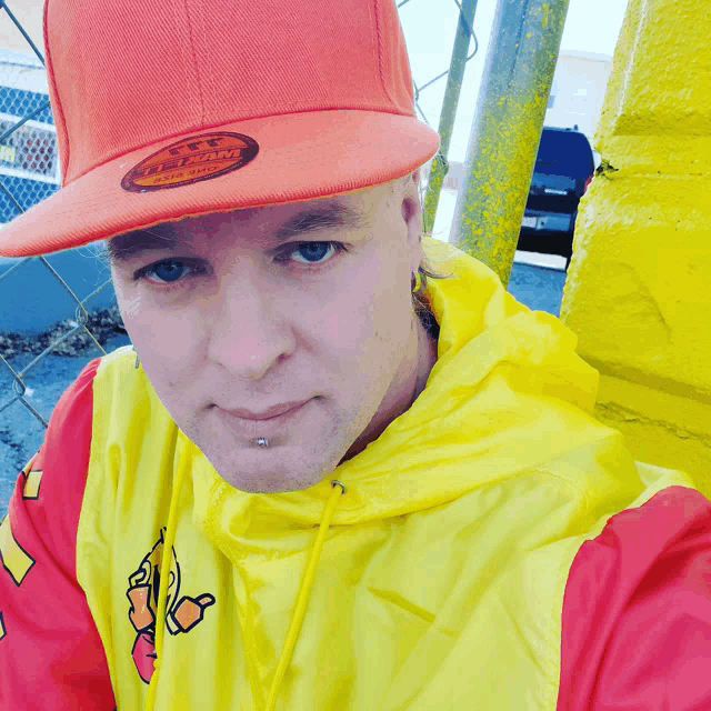 a man wearing an orange hat and a yellow jacket has a piercing on his nose