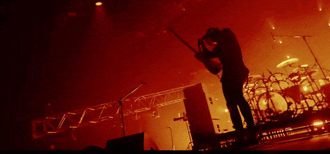 a silhouette of a man playing a guitar in front of a drum set