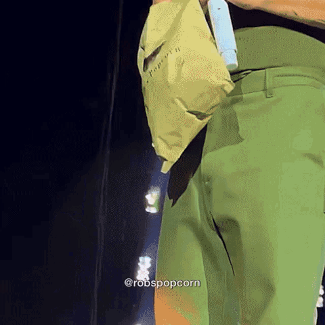 a person wearing green pants is holding a bag on their hip
