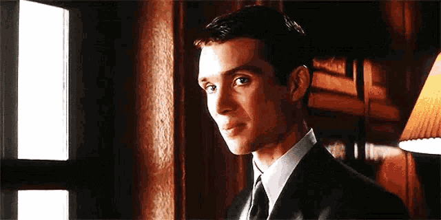 a man in a suit and tie is standing in front of a window and smiling .