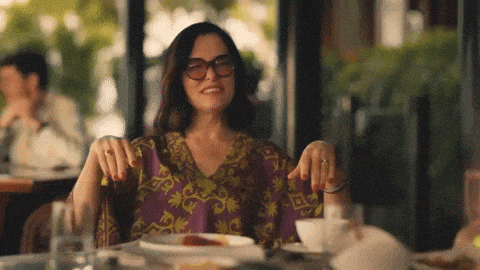 a woman wearing glasses sits at a table with a plate of food on it