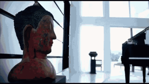 a statue of a buddha sits in a room with a piano