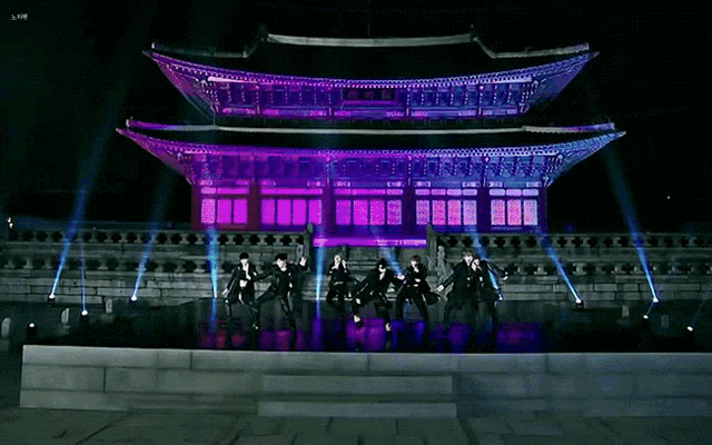 a group of people are dancing in front of a large building with purple lights