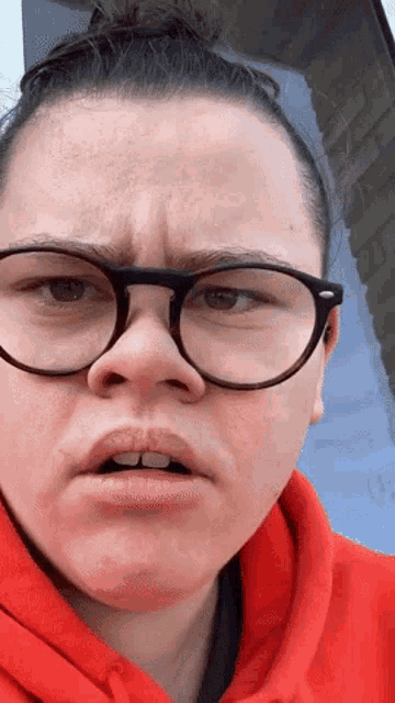 a woman wearing glasses and a red hoodie is making a face