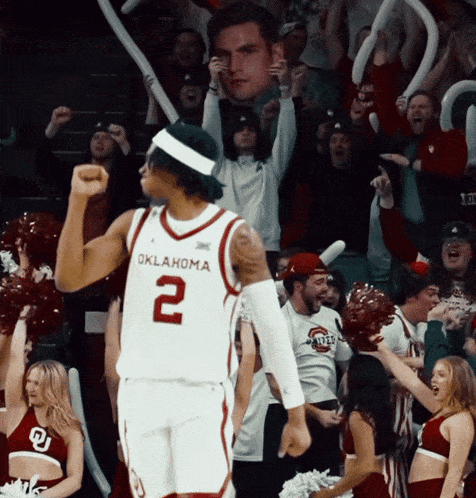 an oklahoma basketball player stands in front of a crowd of cheerleaders