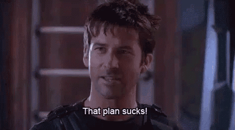 a man in a black shirt is standing in front of a door and says `` that plan sucks '' .