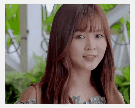 a young woman with long brown hair and bangs is looking at the camera with her tongue out .