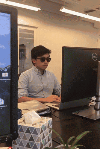 a man wearing sunglasses sits in front of a dell computer monitor