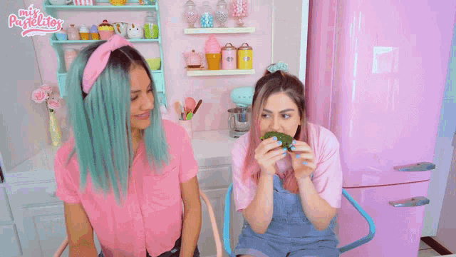 two girls with pink hair and blue nails are eating a green leaf