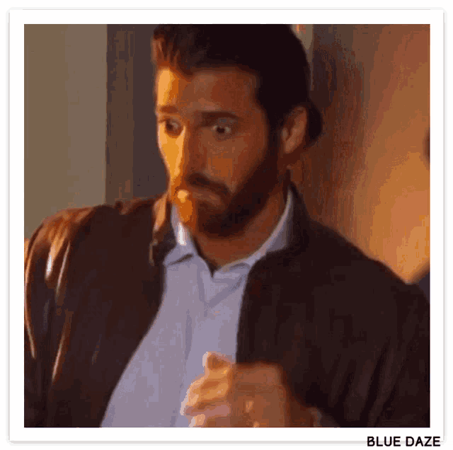 a man with a beard and a leather jacket is standing in front of a door .