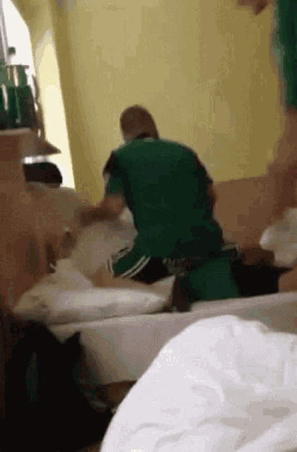 a man in a green shirt is standing on a bed