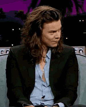 a man with long hair is sitting in a chair laughing .