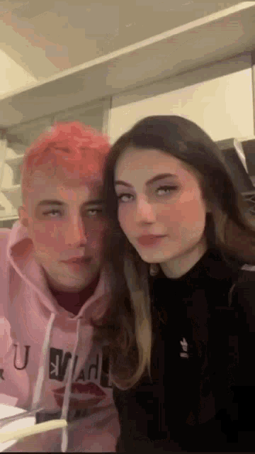 a man and a woman are posing for a picture in a kitchen . the woman has pink hair and the man has red hair .