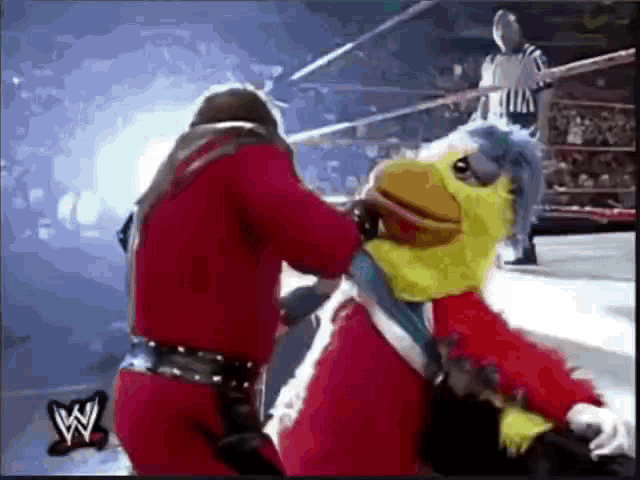 a wrestler is fighting a mascot in a wrestling ring with a referee in the background .