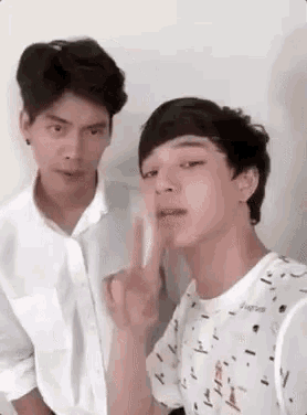 two young men are standing next to each other and one of them is giving the peace sign .