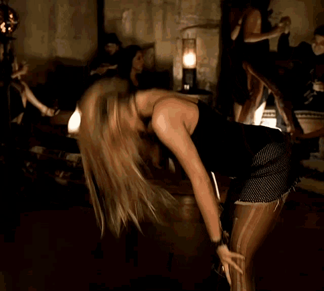 a woman in a black dress stands in a dark room with her hands on her hips