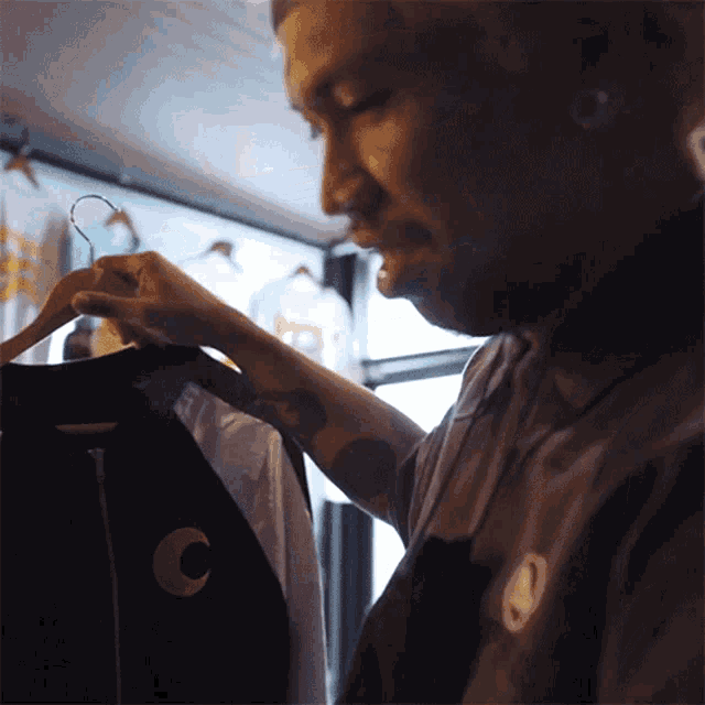 a man with a tattoo on his arm is looking at a shirt with a crescent moon on it