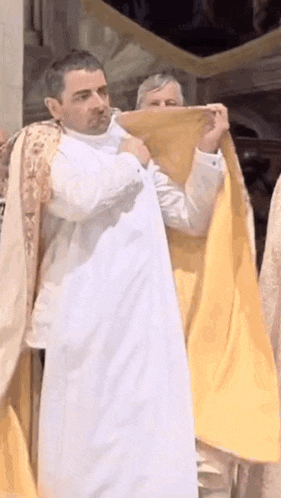a man in a white robe is holding a yellow blanket over his face .