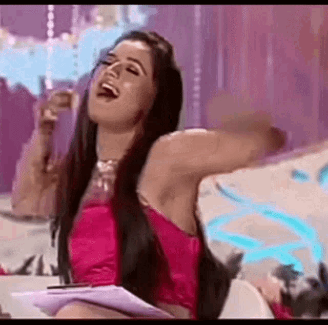a woman in a pink dress is sitting on a couch holding a piece of paper and laughing .