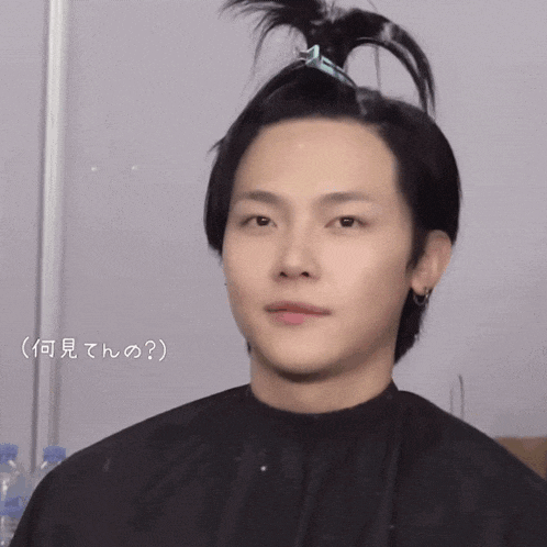 a man with a bun on his head looks at the camera with a smiley face behind him