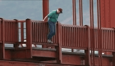 a man in a green shirt is jumping off of a bridge .