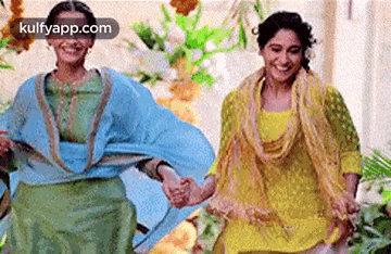 two women in traditional clothing are holding hands and smiling .