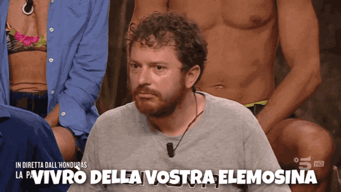 a man with a beard is sitting in front of a group of people and says " vivro della vostra elemosina "