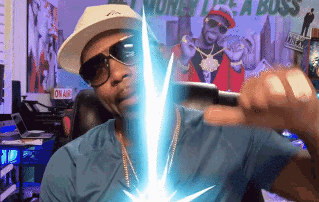 a man wearing a hat and sunglasses is holding a cell phone in front of a poster that says " money like a boss "