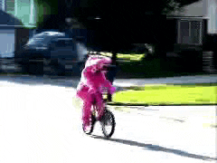 a girl in a pink outfit is riding a bike down the street