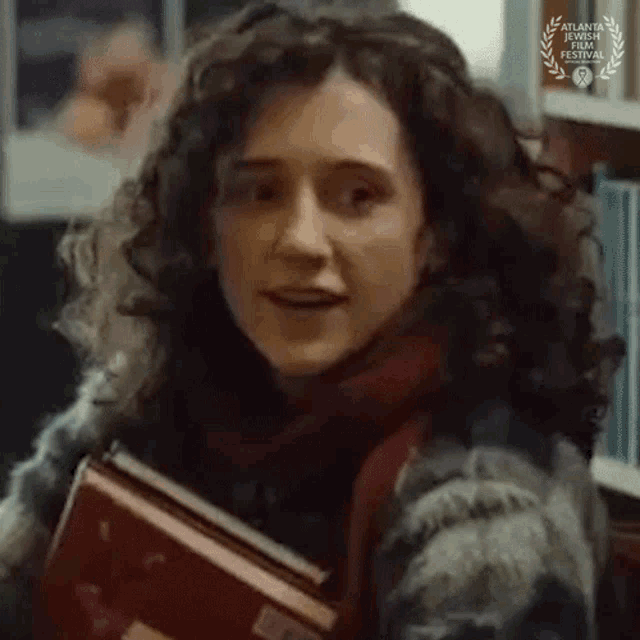 a woman with curly hair is holding a book in a library .